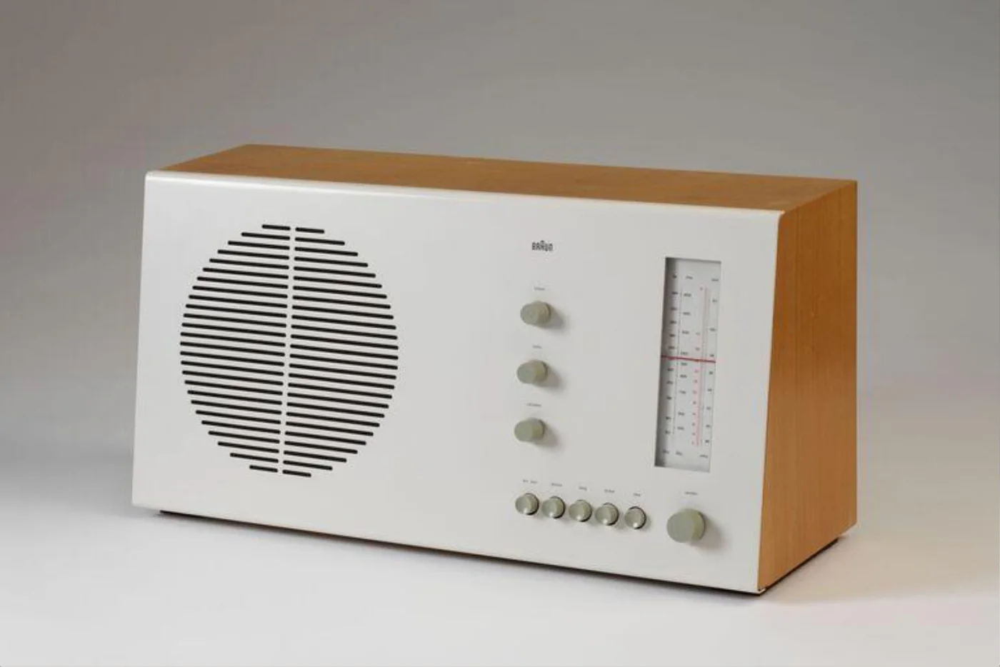 A Braun RT 20 table radio with a white metal face, circular speaker grille, three small knobs, a vertical tuning scale, six buttons, and one larger tuning knob in a beechwood cabinet.