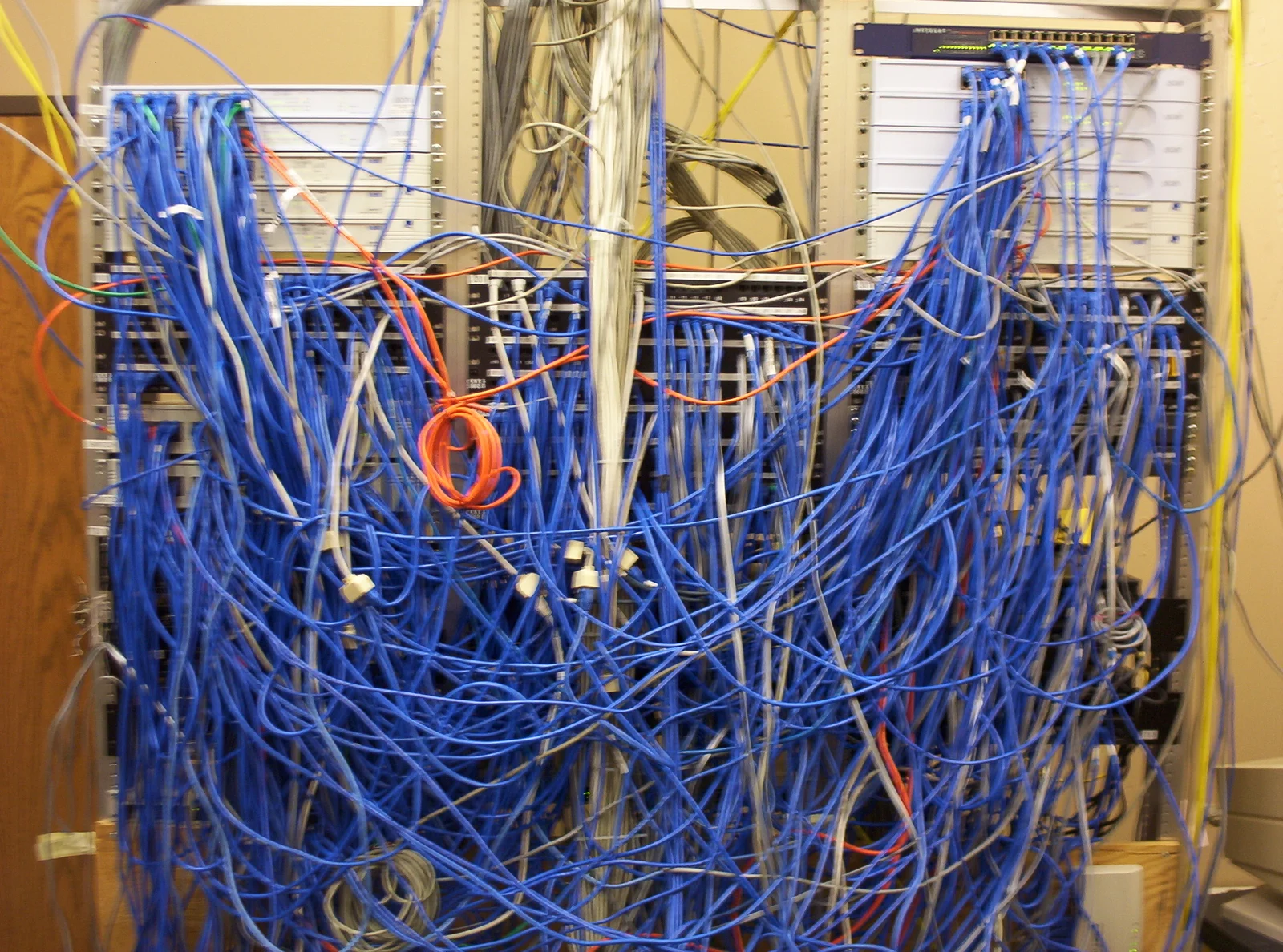 A network closet almost completely obscured by hundreds of tangled blue cables.